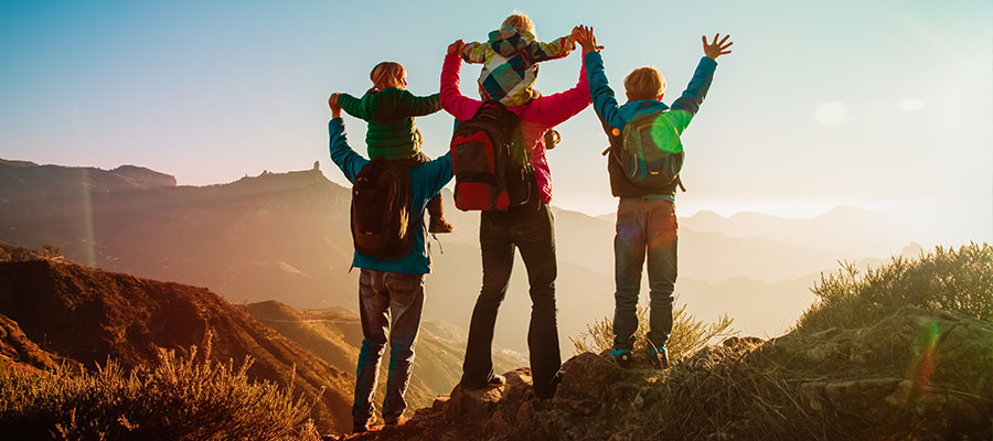 Una familia en una montaña con los brazos extendidos hacia arriba de espalada 