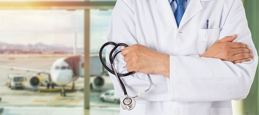 Un médico en un aeropuerto con los brazos cruzados y un estetoscopio en ka mano